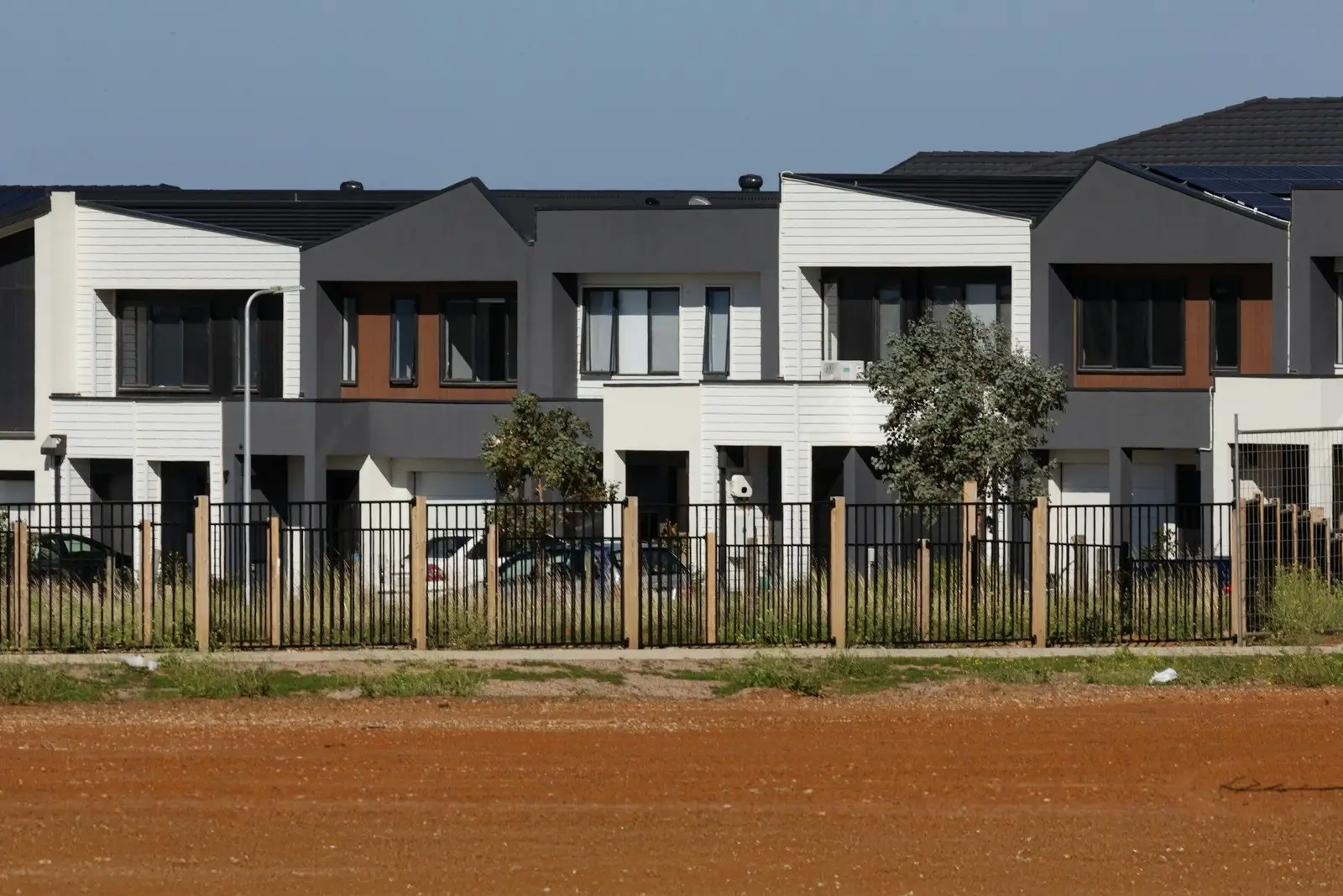 Grey and white townhouses behind a fence and a bare dirt lot