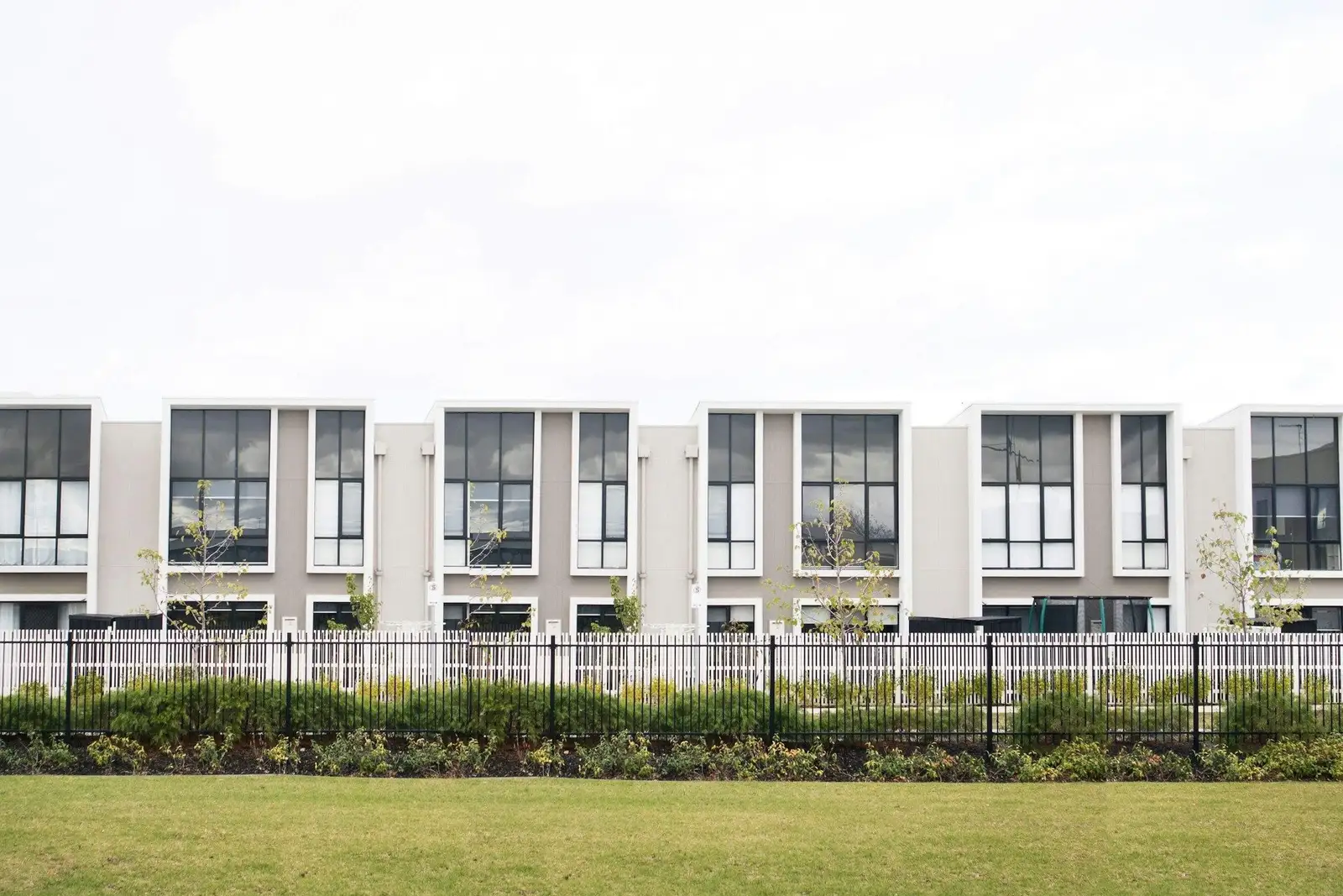 Row of white two-storey townhouses behind a fence and a lawn