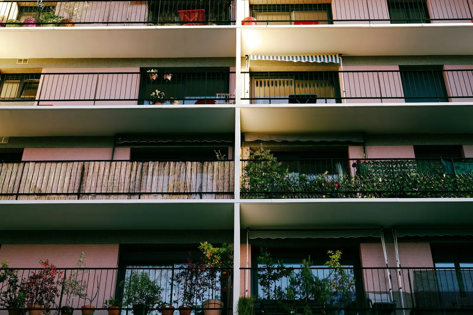 Apartment building balconies with potted plants and pink shutters