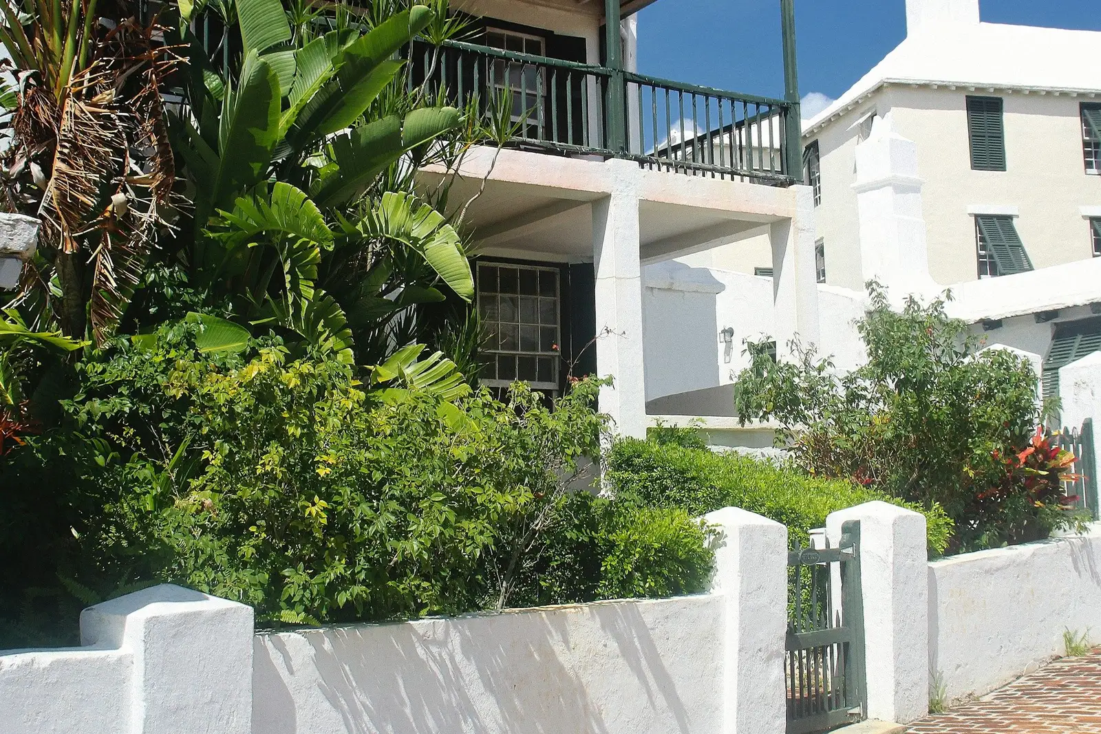 White house with balconies behind a garden wall and tropical plants