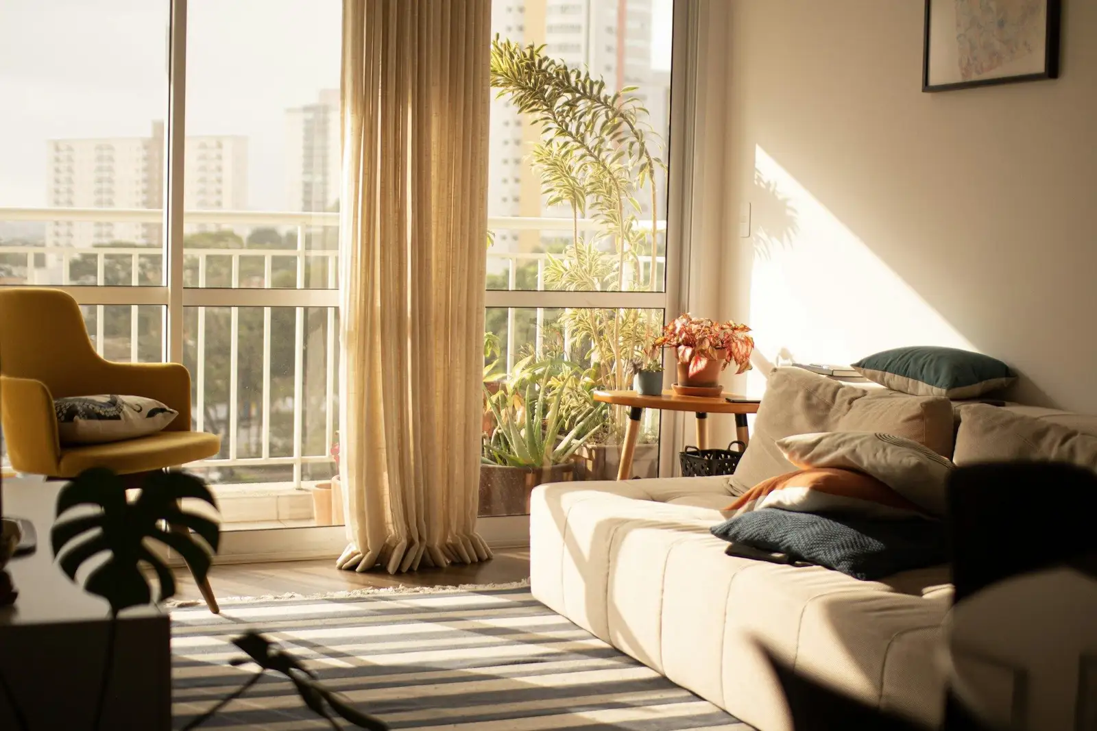 Sunlit living room with a cream sofa and a balcony beyond sheer curtains