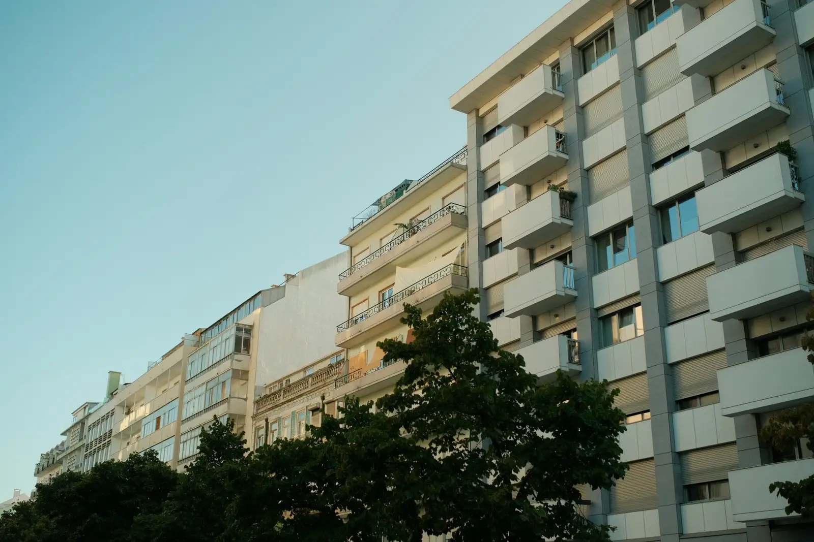 Mid-rise apartment blocks with stacked balconies above trees