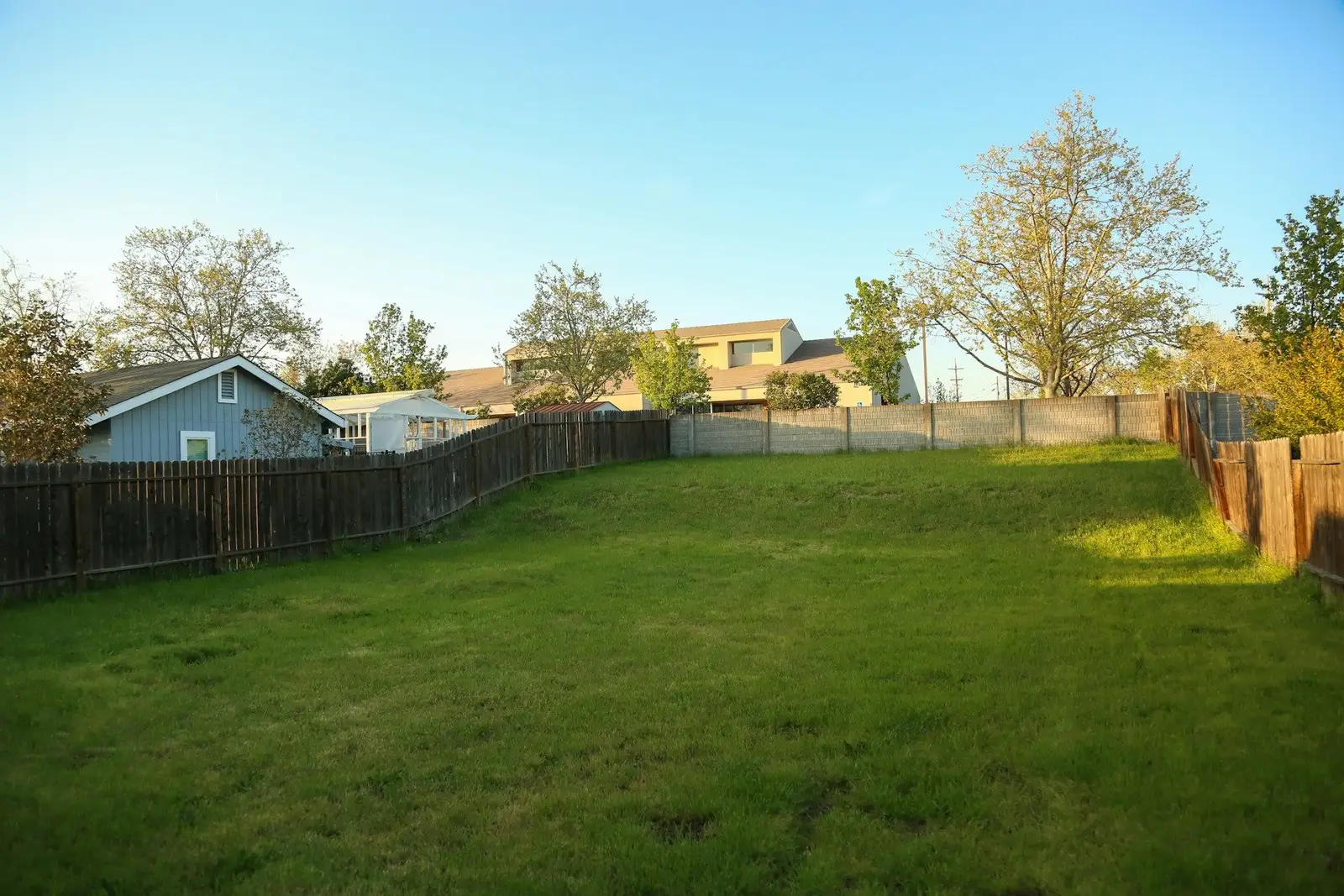 Fenced grassy lot with houses beyond